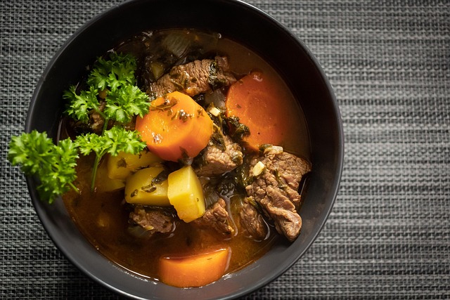 A bowl of beef stew with carrots, potatoes, and fresh greens