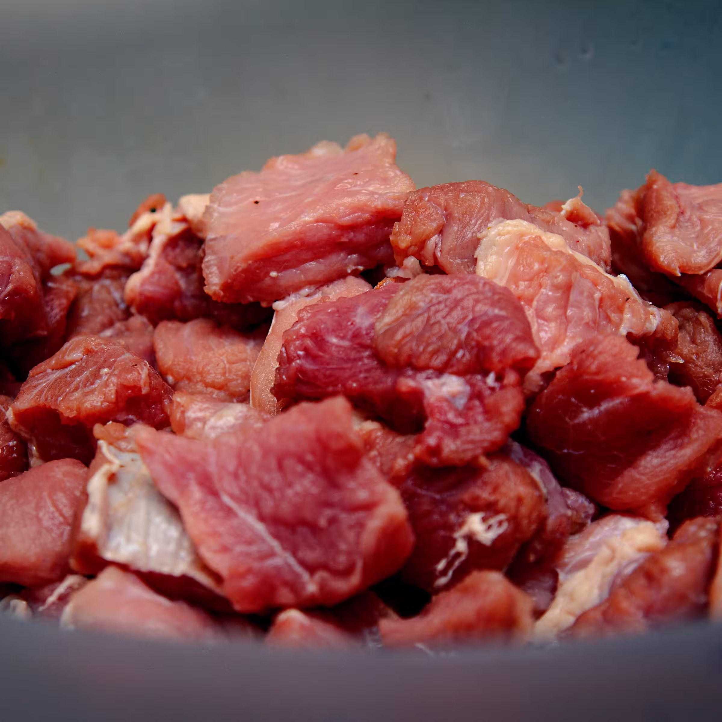 Chunks of well marbled, premium, raw beef piled high in a blue ceramic bowl